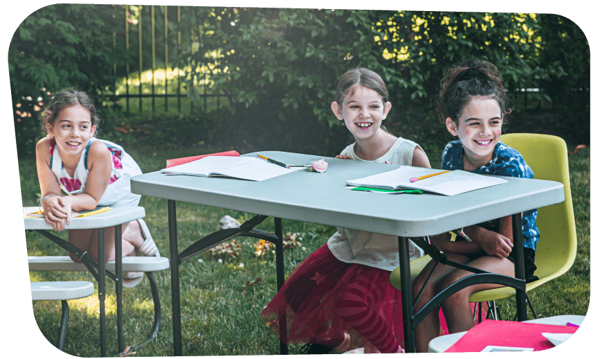 Three girl students sitting at tables outside in their backyard pod